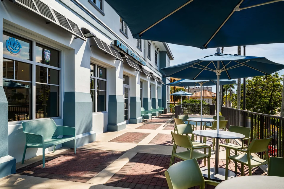 Tables, mint-green chairs, and navy umbrellas along the sunny patio outside Planet.