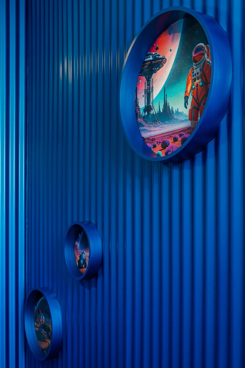 Round space-themed artwork mounted on a ribbed blue wall inside Planet.