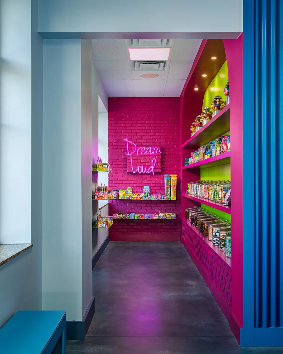 View through a blue doorway into Planet’s candy room, with pink brick walls and lime-green shelves filled with candy.