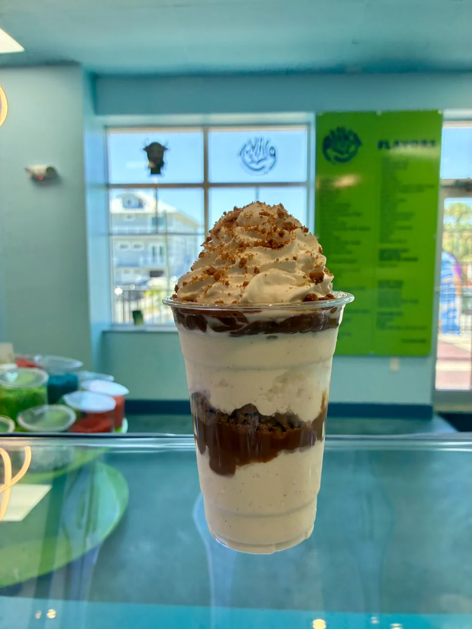 A layered ice cream sundae with brown sauce and a cream topping in a clear cup on the counter inside Planet.
