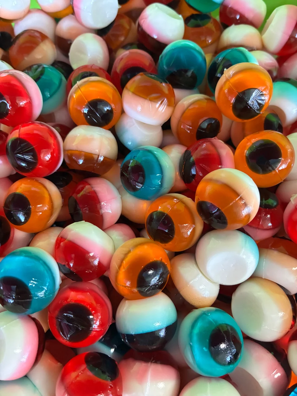 A close-up of glossy gummy eyeballs with white bases and red, orange, blue, and green centers.