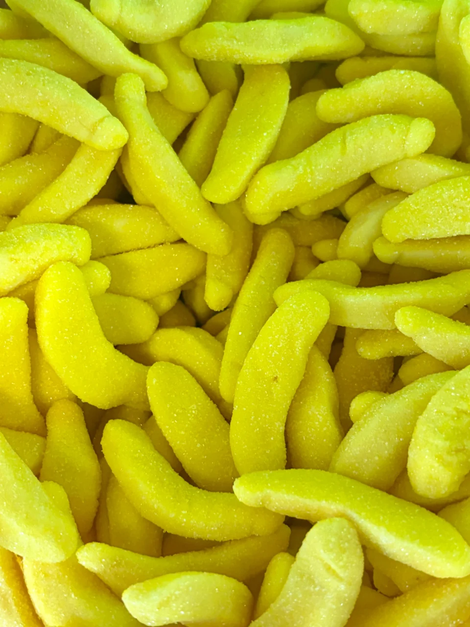 A close-up of bright yellow banana-shaped gummies coated in sugar.