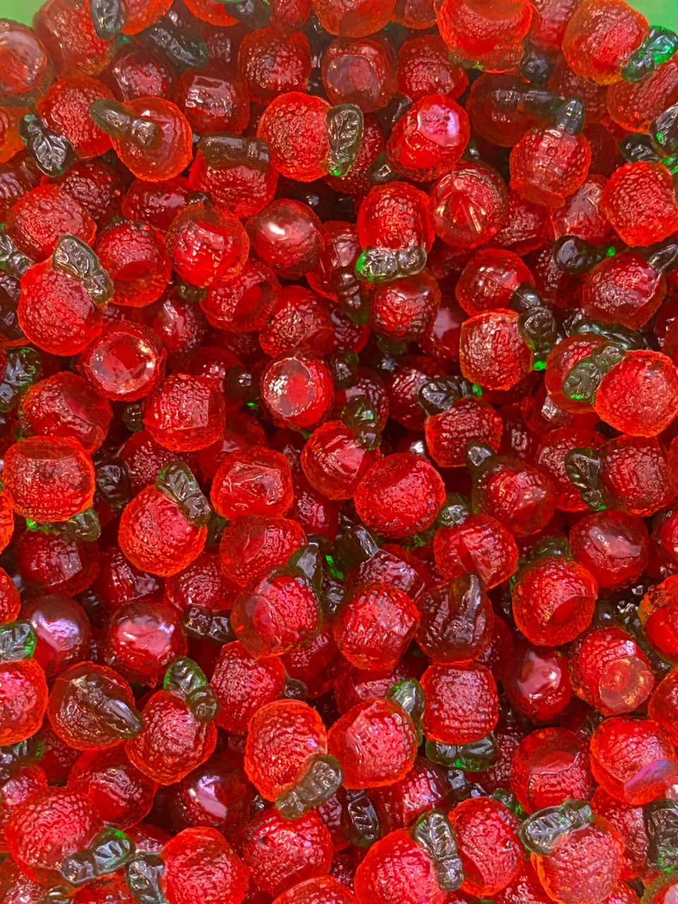 A close-up of translucent red strawberry-shaped gummies with green leaves.